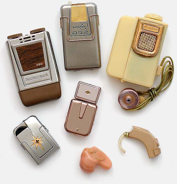 Vintage collectible hearing aids: Top left, Radioear 980 (1967, USA). Top, Radioear 892 (1962, USA). Shown with earphone: Maxitone. Lower left, Audivox Petite (1956, USA). In center with protruding, plug-in microphone, Zenith Crest (1956, USA). Behind-the-ear aid lower right, Zenith (c.1970, USA). In-ear aid, Phonak (c.1990, USA). From 'Hearing Aids' at the web's largest private collection of antiques & collectibles: https://www.ericwrobbel.com/collections/hearing-aids.htm