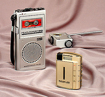 Vintage Olympus Pearlcorders pocket-size tape recorders: the larger one is an early SD model and the small one an L400 from the 1980s. Both are from Japan and use microcassettes. Shown behind is a nifty accessory, the DRA 2 FM tuner which docks to the bottom of the SD, making it an FM radio. What will they think of next? From 'Pocket and Portable Tape Recorders' at the web's largest private collection of antiques & collectibles: https://www.ericwrobbel.com/collections/pocket-recorders.htm